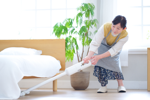 ベッドの下を掃除機掛けする女性